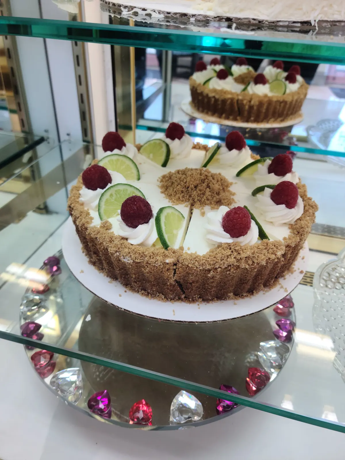 Key lime pie topped with whipped cream, lime slices and raspberries in the display case