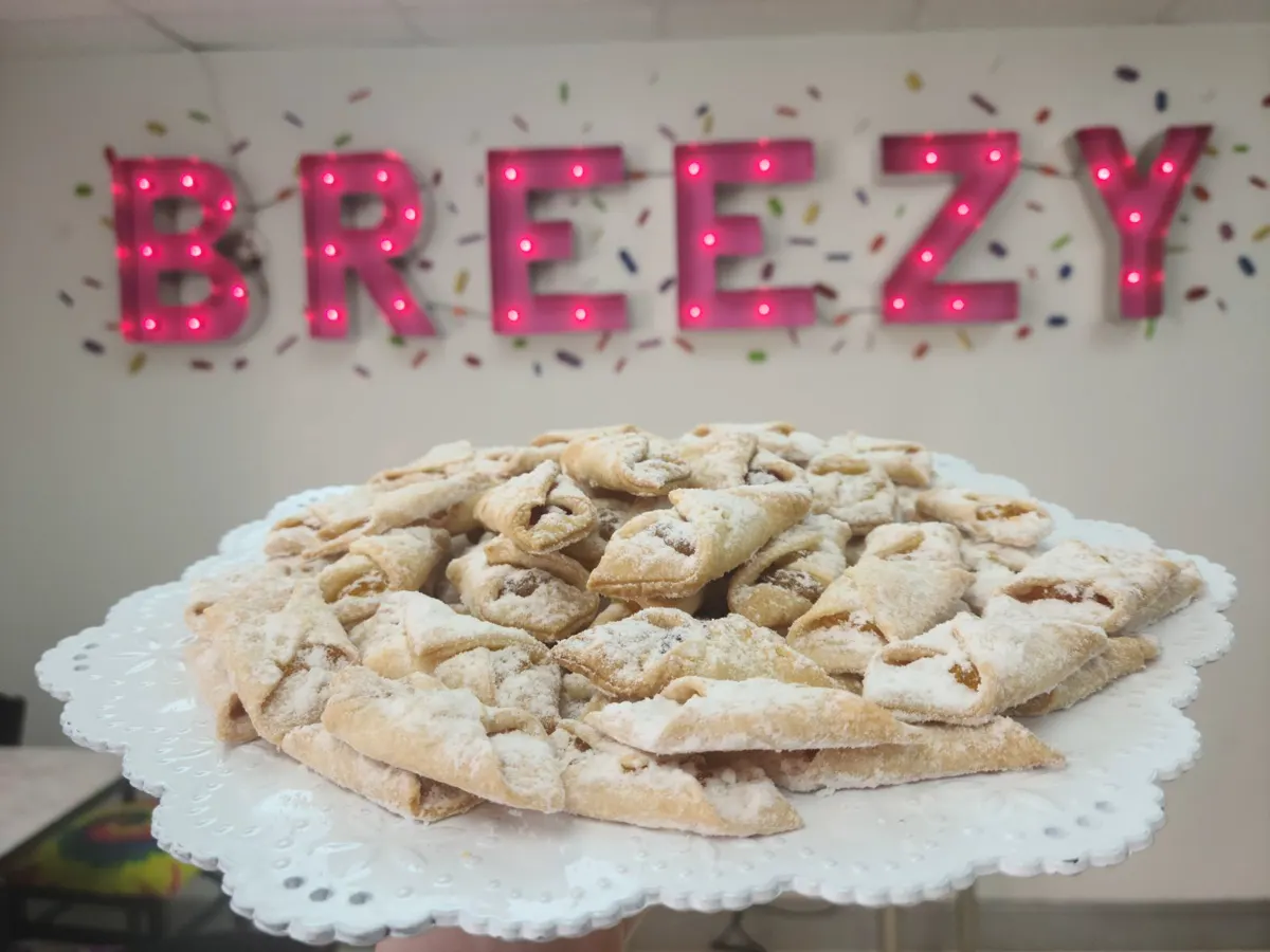 A platter of powdered pastries in front of the pink marquee BREEZY sign inside the shop